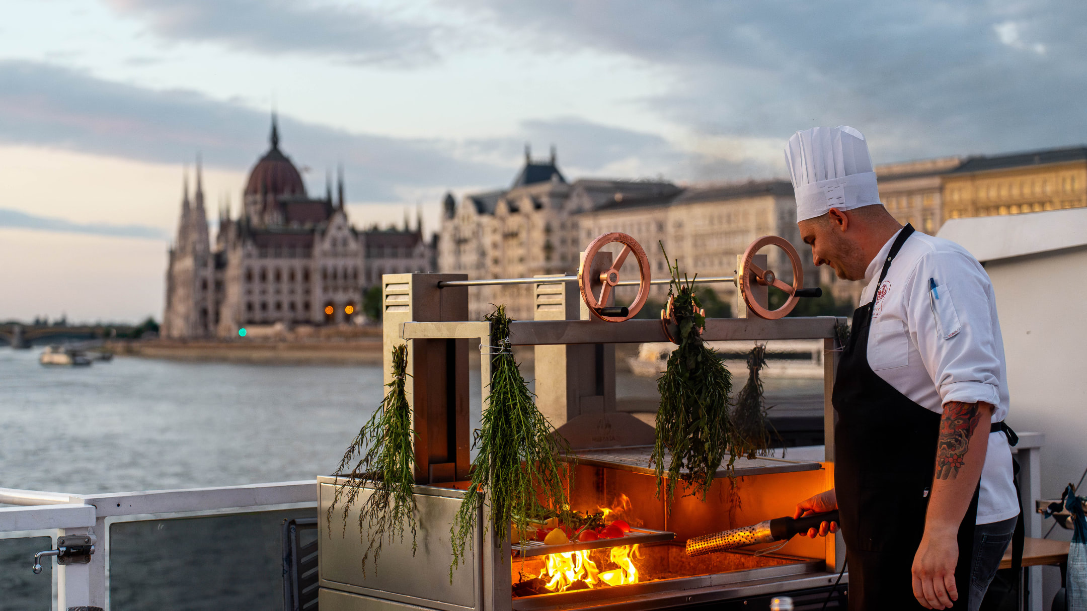 Chef grilling on the open deck with the Hungarian Parliament in the background